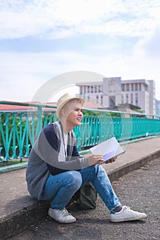 Young Asian reading book while siting on city walking brigde.