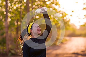 Young Asian runner girl refreshing drinking and pouring water on her head. Attractive and happy Korean woman tired after running