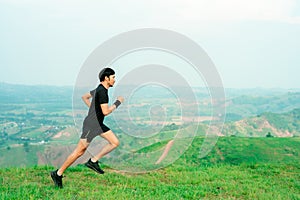 Young Asian runner, wearing black sportswear, running on a big mountain trail, cool morning, windmills, and sky in the background