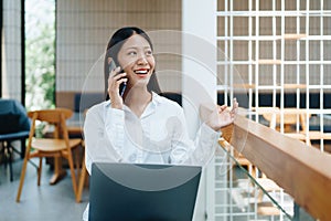 A young Asian self employed woman showing a smiling face and happiness while using a computer and using smartphone