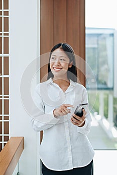 A young Asian self employed woman showing a smiling face and happiness while using smartphone mobile talking business