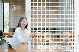 A young Asian self employed woman showing a smiling face and happiness while using smartphone mobile talking business