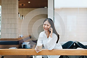 A young Asian self employed woman showing a smiling face and happiness while using smartphone mobile talking business