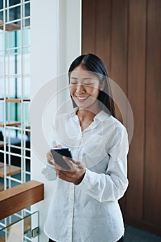 A young Asian self employed woman showing a smiling face and happiness while using smartphone mobile talking business