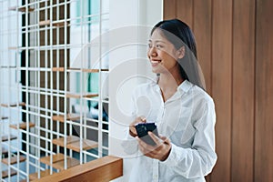A young Asian self employed woman showing a smiling face and happiness while using smartphone mobile talking business