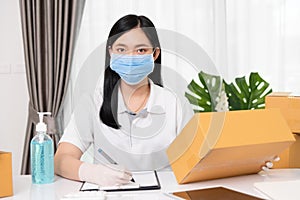 Young Asian small business owner wearing face mask protective to carrying product boxes at home office, startup SME entrepreneur