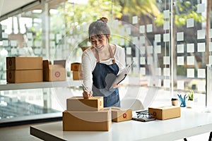 Young Asian small business owner working at home office, taking note on purchase orders. Online marketing packaging