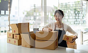 Young Asian small business owner working at home office, taking note on purchase orders. Online marketing packaging