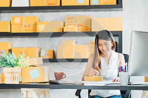 Young Asian small business owner working at home office, taking note on purchase orders. Online marketing packaging delivery