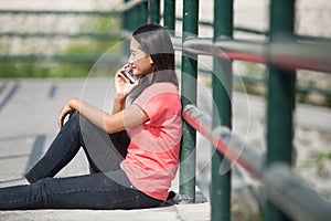 Young Asian student outdoor, talking on the phone while sitting