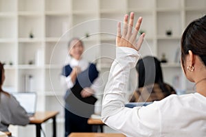 A young Asian student raising her hand to ask a question to her teacher in the classroom, studying