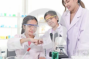 Young Asian student schoolgirls in lab coat bumping fists together to celebrate success of science experiment at laboratory.