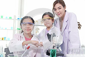 Young Asian student schoolgirls in lab coat bumping fists together to celebrate success of science experiment at laboratory.
