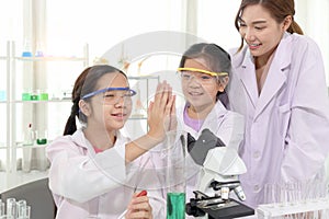 Young Asian student schoolgirls in lab coat give high five clap hands to celebrate success of science experiment at laboratory.