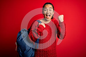 Young asian student woman wearing backpack standing over isolated red background screaming proud and celebrating victory and