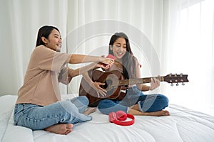 Young asian teen and her friend sing and playing guitar using mobile phone as a microphone, enjoy leisure weekend at home. Stress