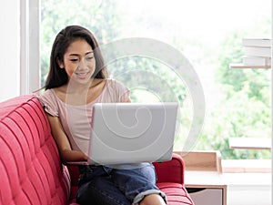 Young asian teen use laptop computer on the red sofa to relax in the living room