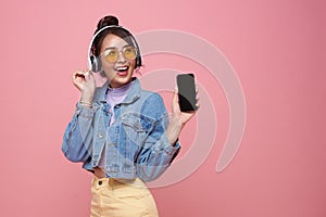 Young Asian teen woman showing smart phone she listening music in headphones isolated on pink background