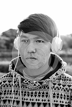 Young Asian teenage boy wearing headphones while relaxing at the park