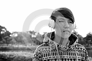 Young Asian teenage boy wearing headphones while relaxing at the park