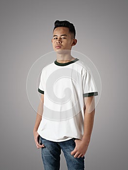 Young Asian teenage boy wearing white ringer shirt, standing with hands on hip over gray background, t-shirt template