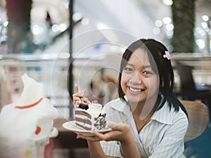 Young Asian teenage girl eating chocolate cake happily. Concept of teenage health and nutrition