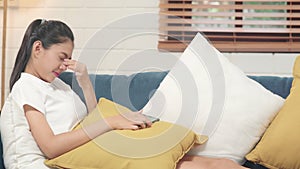 Young Asian teenager woman rubbing her eyes feel painful after playing mobile phone while lying on sofa in living room. Lifestyle