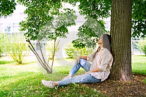 Young Vietnamese woman sitting relaxing in shadow under green tree on sunny day