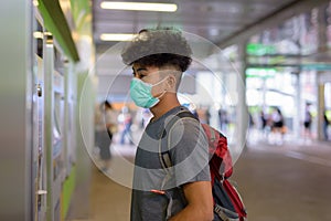 Young Asian tourist man as backpacker with mask buying ticket at the sky train station