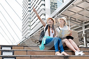 Young Asian tourist woman pointing into distance while her friend looking with smiling faces