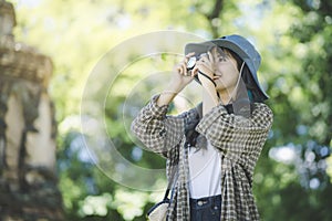 Young Asian traveler woman taking photo by her camera while traveling around Thai ancient temple on holidays vacation