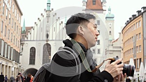 Young Asian traveling backpacker in city centre in Europe. Man taking photos in Marienplatz square, Munich, Germany