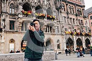 Young Asian traveling backpacker in city centre in Europe. Man taking photos in Marienplatz square, Munich, Germany