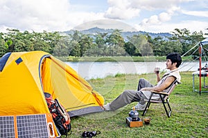 Young Asian traveling man relax and enjoy outdoor lifestyle camping in forest mountain on summer holiday travel vacation.