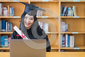 A young Asian university graduate woman in graduation gown expressing joy and excitement to celebrate her education achievement in
