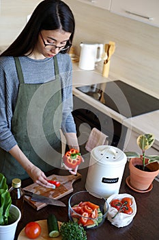 Young Asian vegan woman cleans vegetables and throws waste into a compost bin. Eco friendly person