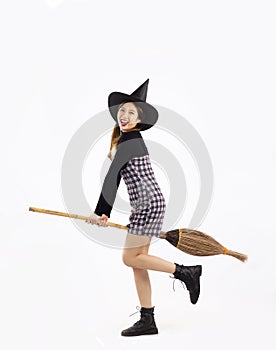 Young asian witch girl in black halloween costume wearing witch hat and holding broom smiling and posing on white background
