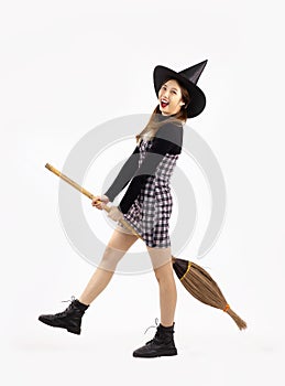 Young asian witch girl in black halloween costume wearing witch hat and holding witch broom posing on white background