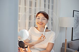 Young Asian woman apply blush on a cheekbone with a brush photo