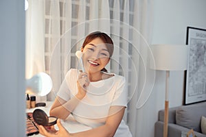 Young Asian woman apply blush on a cheekbone with a brush photo
