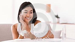 Young asian woman applying cream on her face