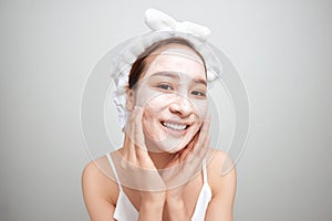 Young Asian woman applying facial clay mask over white background. Beauty treatments concept
