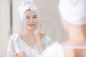 Young asian woman applying foundation or moisturizer on her face in front of mirror