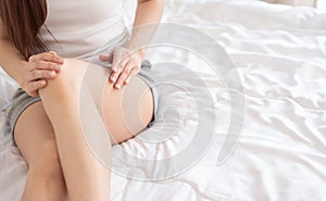 Young Asian woman applying smooth body lotion on her legs while sitting in bed at her bedroom