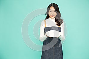 Young Asian woman in apron standing and holding empty white plate or dish  on green background