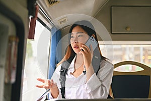 Young Asian woman with backpack talking on mobile phone inside public transport bus.