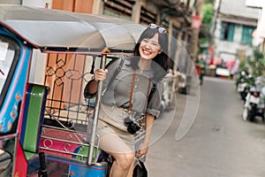 Young Asian woman backpack traveler standing a side of Tuk Tuk taxi on summer vacations at Bangkok, Thailand