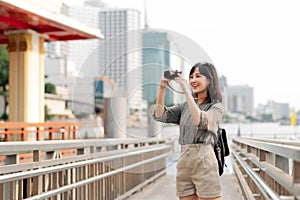 Young Asian woman backpack traveler using a camera in express boat pier on Chao Phraya River in Bangkok