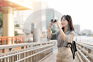 Young Asian woman backpack traveler using a camera in express boat pier on Chao Phraya River in Bangkok