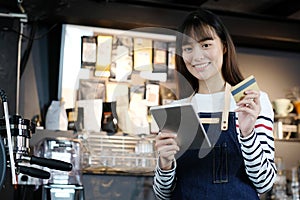 Young asian woman barista using tablet and holding credit card a